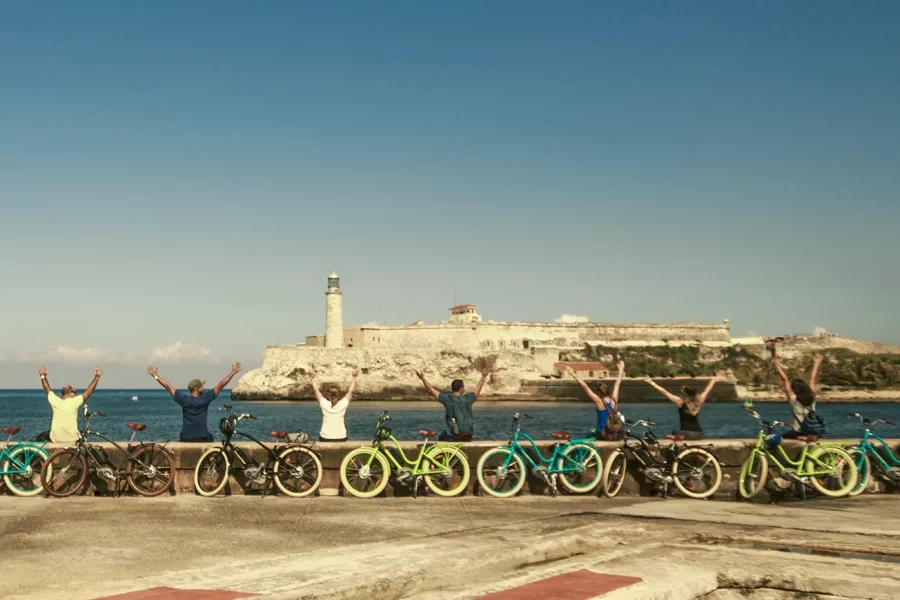 Petit groupe de personnes à vélo le long de la côte, avec vue sur la mer et le phare historique dans le port de La Havane, Cuba.